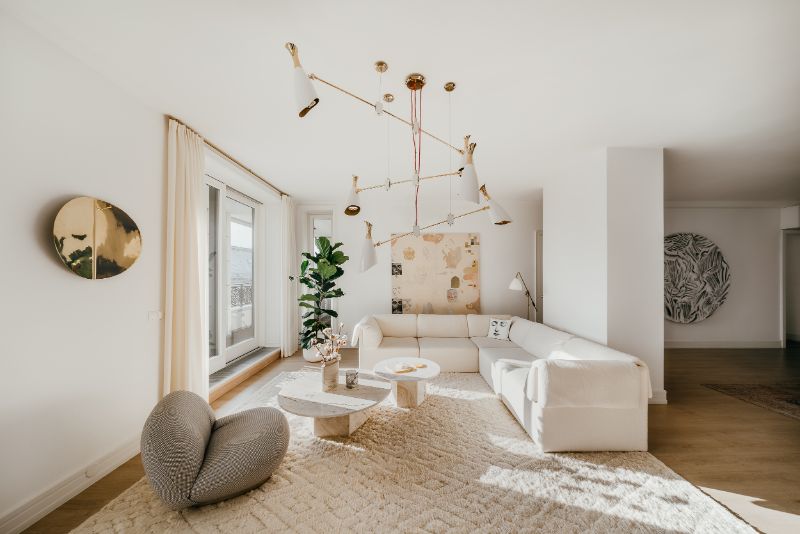 White living room with a large white area rug, white sofa, gray armchair and center table in marble. There is gold hanging lights